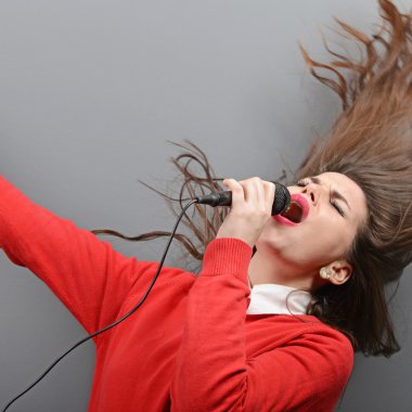 Güzel kadının gri backgro karşı mikrofon ile şarkı