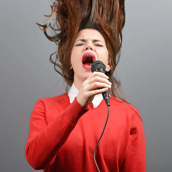 Beautiful woman singing with the microphone against gray backgro — Stock Photo, Image