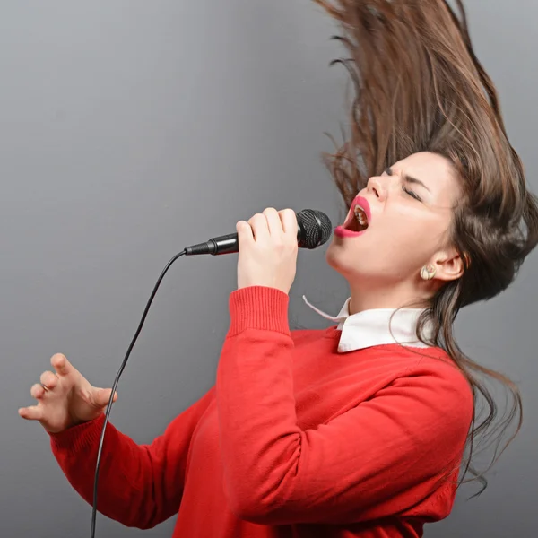 Hermosa mujer cantando con el micrófono contra el backgro gris — Foto de Stock