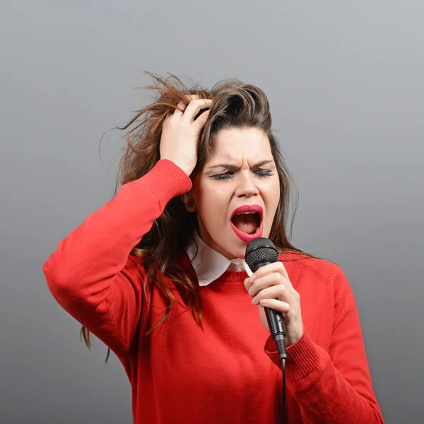 Schöne Frau singt mit dem Mikrofon gegen grauen Backgro — Stockfoto