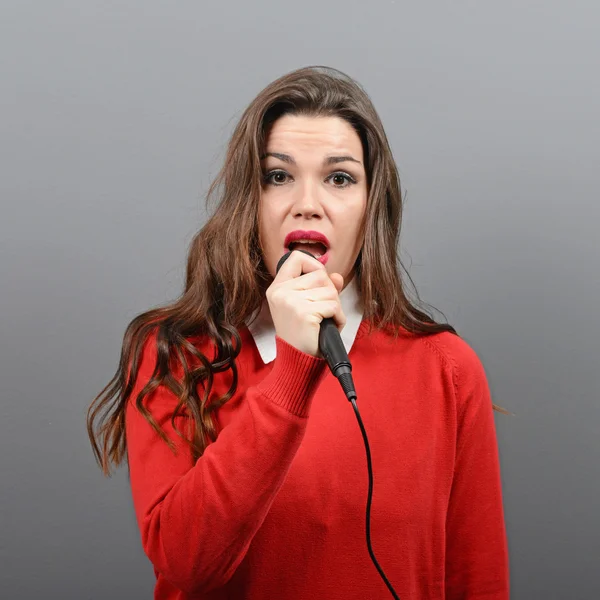 Beautiful woman singing with the microphone against gray backgro — Stock Photo, Image