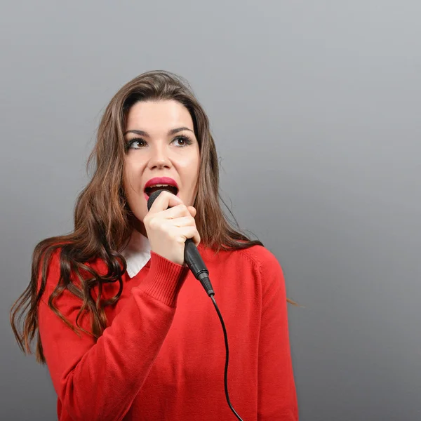 Hermosa mujer cantando con el micrófono contra el backgro gris —  Fotos de Stock