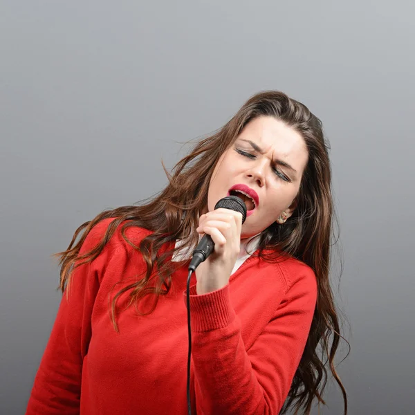 Красива жінка співає з мікрофоном проти сірого фону — стокове фото