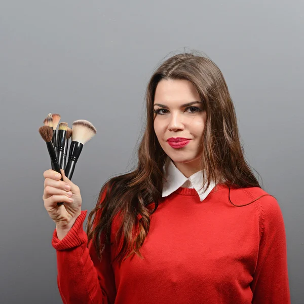 Portrait of woman holding make-up brushes against gray backgroun — Stock Photo, Image