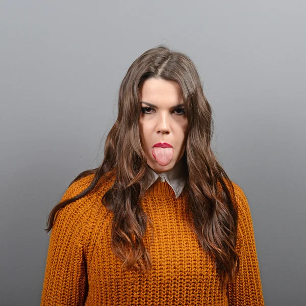 Portrait of woman sticking out her tongue against gray backgroun — Stock Photo, Image