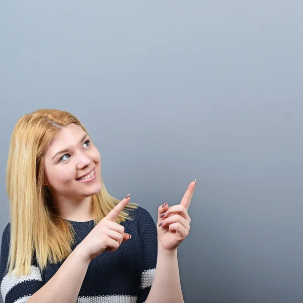 Hermosa mujer señalando el área en blanco contra el fondo gris — Foto de Stock