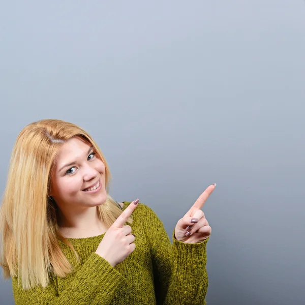 Beautiful woman pointing to blank area against  gray background — Stock Photo, Image