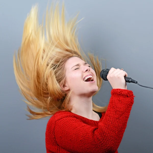 Hermosa mujer cantando con el micrófono contra el backgro gris — Foto de Stock