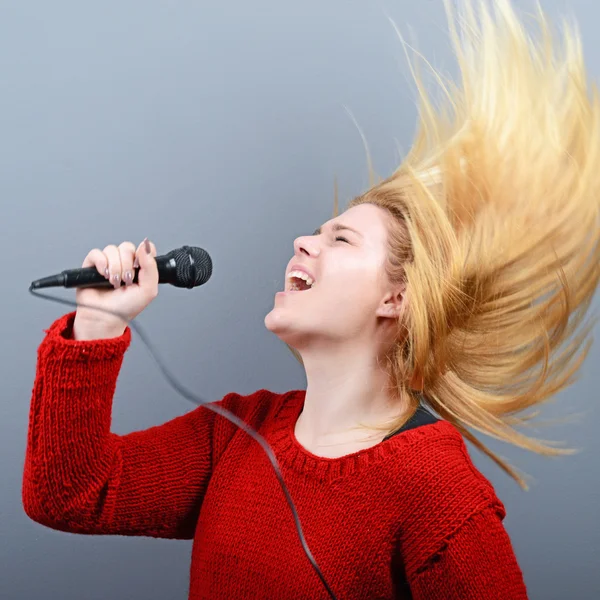 Mooie vrouw zingen met de microfoon tegen de grijze backgro — Stockfoto