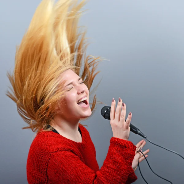 Όμορφη γυναίκα που τραγουδά με το μικρόφωνο κατά γκρι backgro — Φωτογραφία Αρχείου