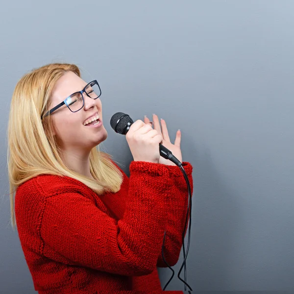 Schöne Frau singt mit dem Mikrofon gegen grauen Backgro — Stockfoto