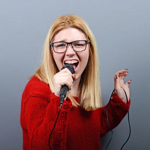 Όμορφη γυναίκα που τραγουδά με το μικρόφωνο κατά γκρι backgro — Φωτογραφία Αρχείου