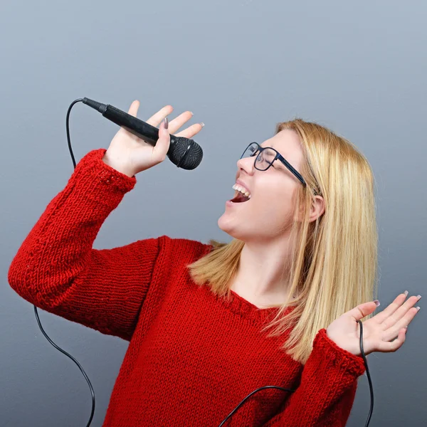 Mulher bonita cantando com o microfone contra backgro cinza — Fotografia de Stock