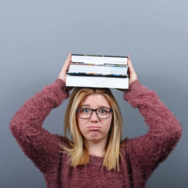 Portrait of a young student woman holding books on head against — Stock Photo, Image