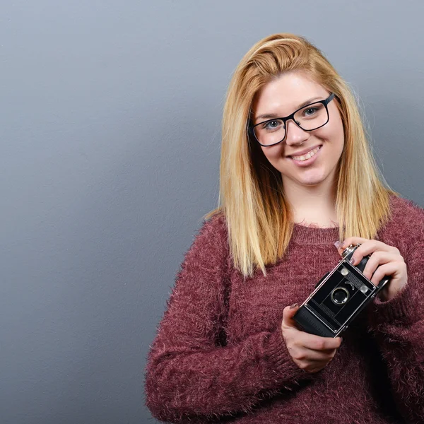 Portrait of a young woman holding retro camera against gray back