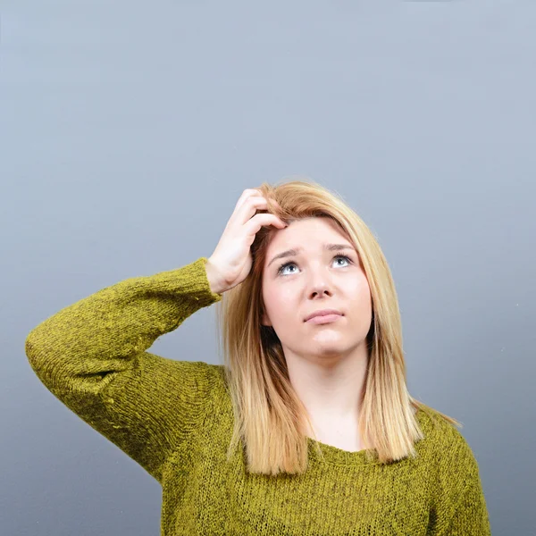 Portrait of forgetful young woman against gray background — Stock Photo, Image