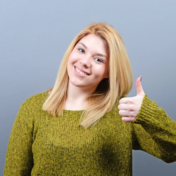 Retrato de mujer feliz sosteniendo pulgares contra fondo gris — Foto de Stock