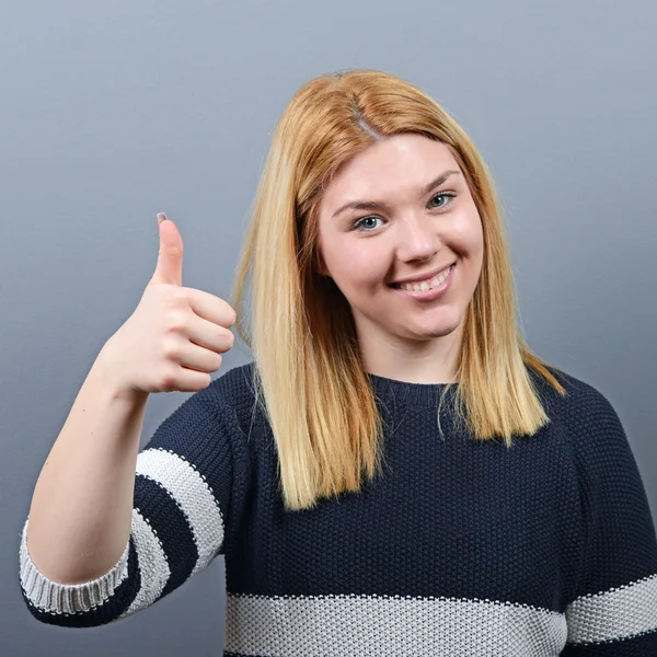 Portrait of happy woman holding thumbs up against gray backgroun — Stock Photo, Image