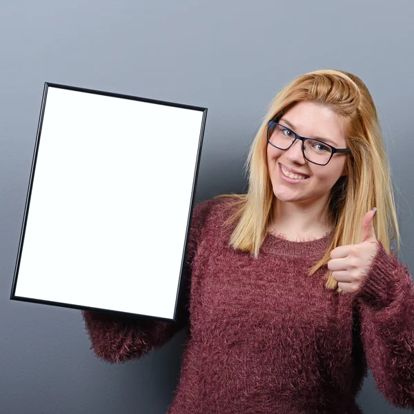 Portrait of woman holding blank sign board with thumb up against — Stock Photo, Image