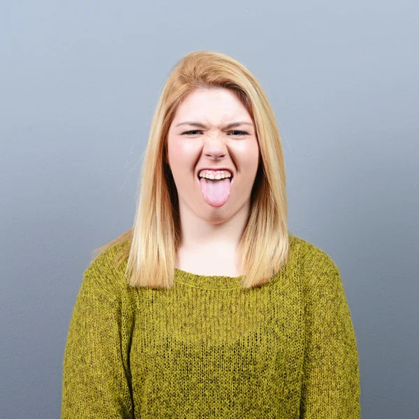 Retrato de mujer sobresaliendo de su lengua contra fondo gris — Foto de Stock