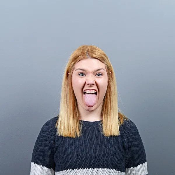Retrato de mujer sobresaliendo de su lengua contra fondo gris — Foto de Stock