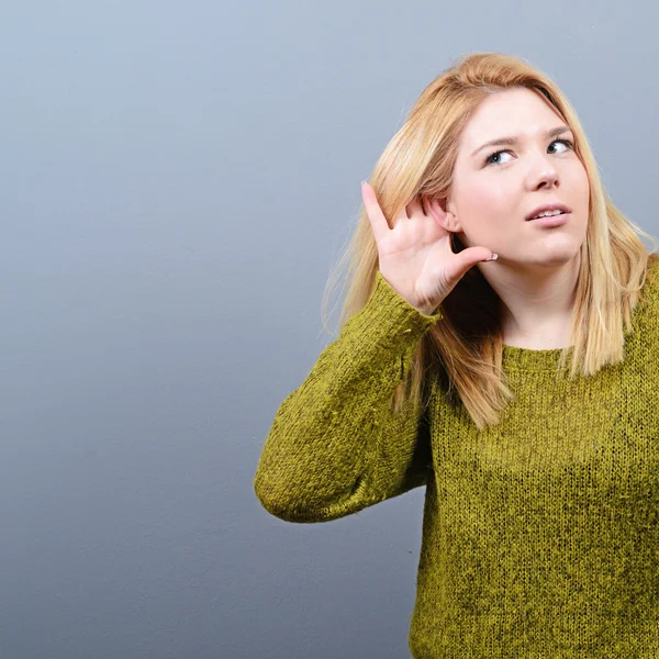 Porträt einer Frau, die versucht, etwas gegen grauen Backgr zu hören — Stockfoto