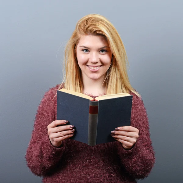 Portrait of young woman reading book against gray background — Stock Photo, Image