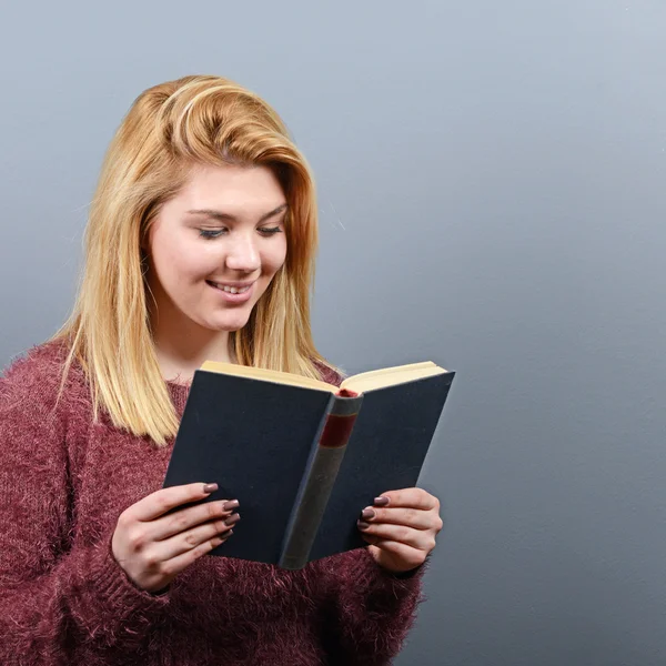 Retrato de jovem mulher lendo livro contra fundo cinza — Fotografia de Stock