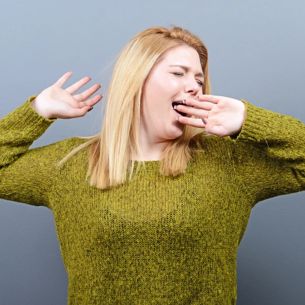 Portret van de jonge vrouw die zich uitstrekt en geeuwen tegen grijze rug — Stockfoto