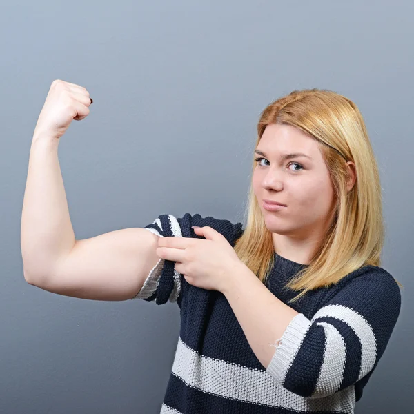 Pretty young brunette woman showing bicep on her arm against gra — Stock Photo, Image