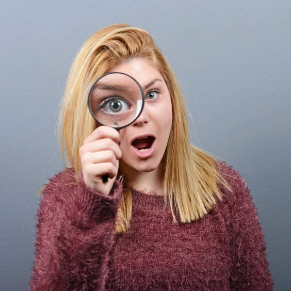 Woman with magnifying glass against gray background — Stock Photo, Image