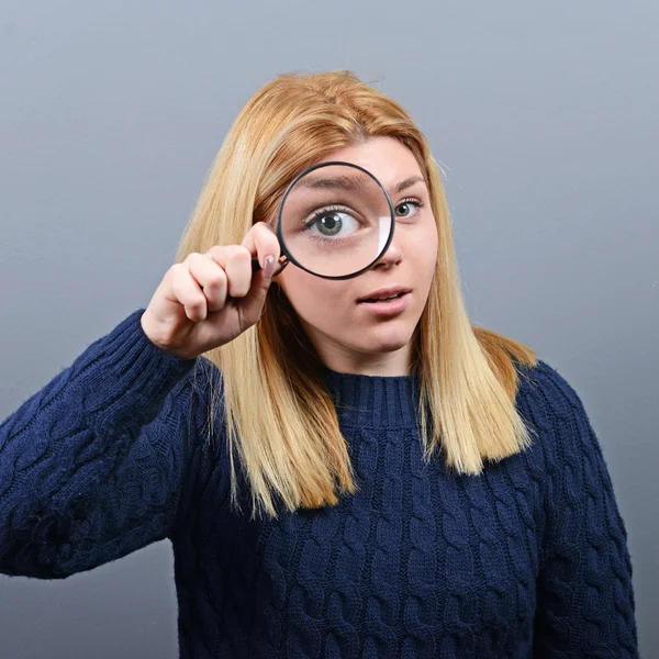 Woman with magnifying glass against gray background — Stock Photo, Image