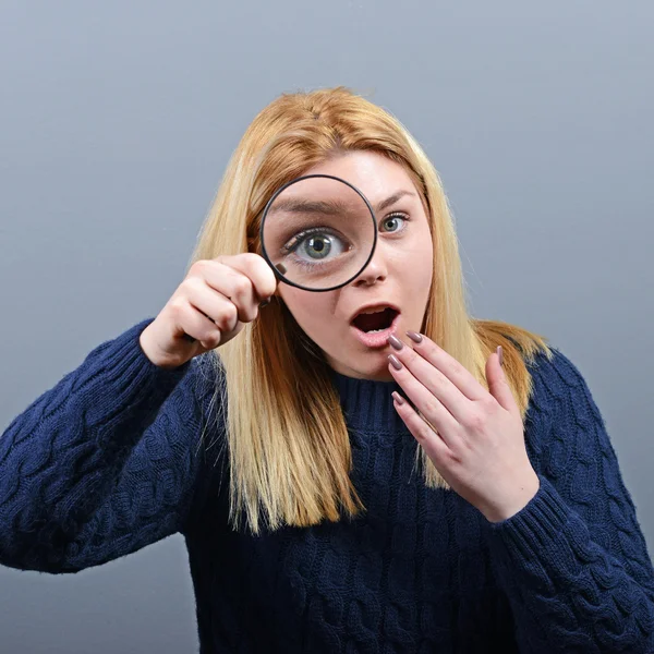 Woman with magnifying glass against gray background — Stock Photo, Image