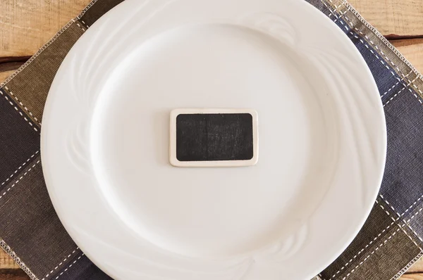 Blank signboard with empty white plate on wooden table — Stock Photo, Image