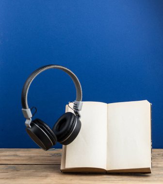 Kitaplı kulaklıklar havada uçuşuyor. Koyu mavi bir arkaplanda. 