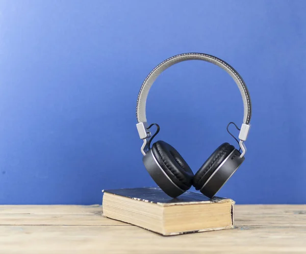 Audio book concept. Headphones and book over wooden table. Space for your text
