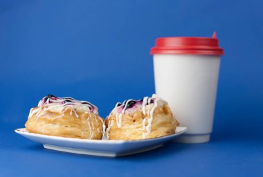 Tek kullanımlık sıcak kahve ve mavi arka planda tatlı hamur işleri. Kahve zamanı, kahvaltı.