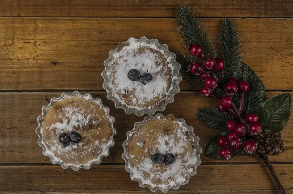 木製のテーブルの上に粉砂糖とクリスマスの装飾で飾られた休日のカップケーキ トップ表示 — ストック写真