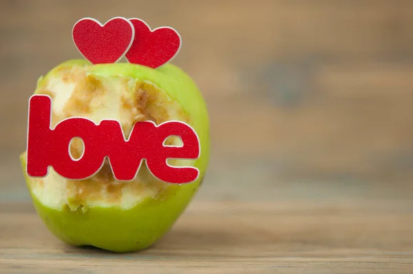 old paul-a bitten green apple with a red heart on wood background.