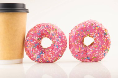 Beyaz arka planda tek kullanımlık kahve fincanı olan iki lezzetli çörek.