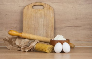 Kağıt torbada makarna, yumurta, un ve tahta masa üzerinde merdane.