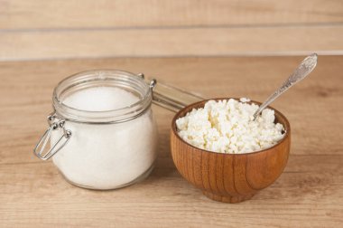 Cam kavanoz şeker ve ahşap mutfak masasında süzme peynirli ahşap kase.