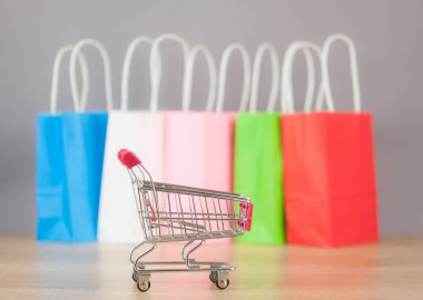 Vagon arabası ve ahşap masa arkasında renkli alışveriş torbaları. İnternetten alışveriş yapma fikri, yaz indirimi, süpermarket, indirim promosyonu ve Kara Cuma konsepti. Metin için alanı kopyala.