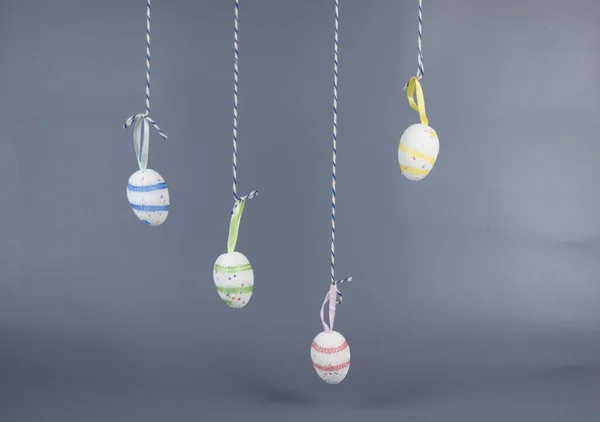 Home decor for Easter. Bright Easter eggs hanging on strings on a gray background, copy space