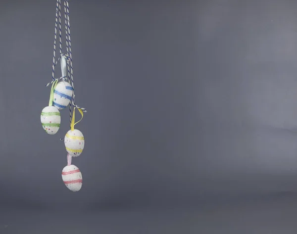 Home decor for Easter. Bright Easter eggs hanging on strings on a gray background, copy space