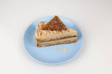 Beyaz bir zemin üzerine seramik tabakta kremalı bademli kek dilimi.