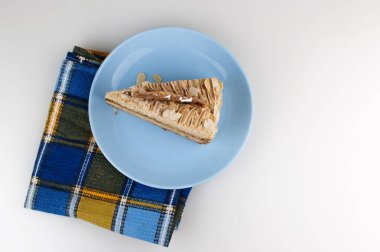 Beyaz bir zemin üzerine seramik tabakta kremalı bademli kek dilimi.