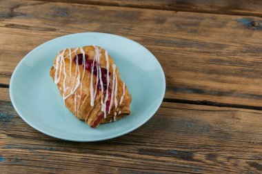 Doğal ahşap tahtalardan yapılmış bir masanın üzerinde kirazlı çörekli seramik bir tabak var. Kahvaltı.