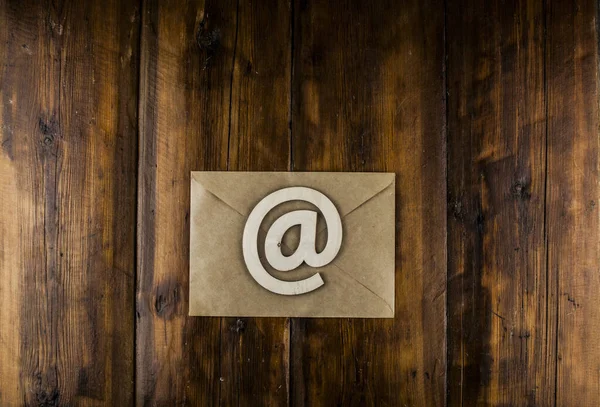 手工信封上的一个电子邮件标识放在一张老式木制桌子上 概念电子邮件消息信 带有复制空间的顶部视图 — 图库照片
