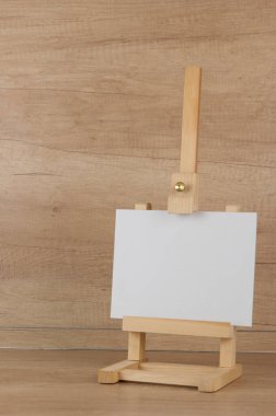 Hafif ahşap zemin üzerinde küçük bir sehpa üzerinde beyaz tuval, yakın, kopya alanı ile boş sayfa kavramı